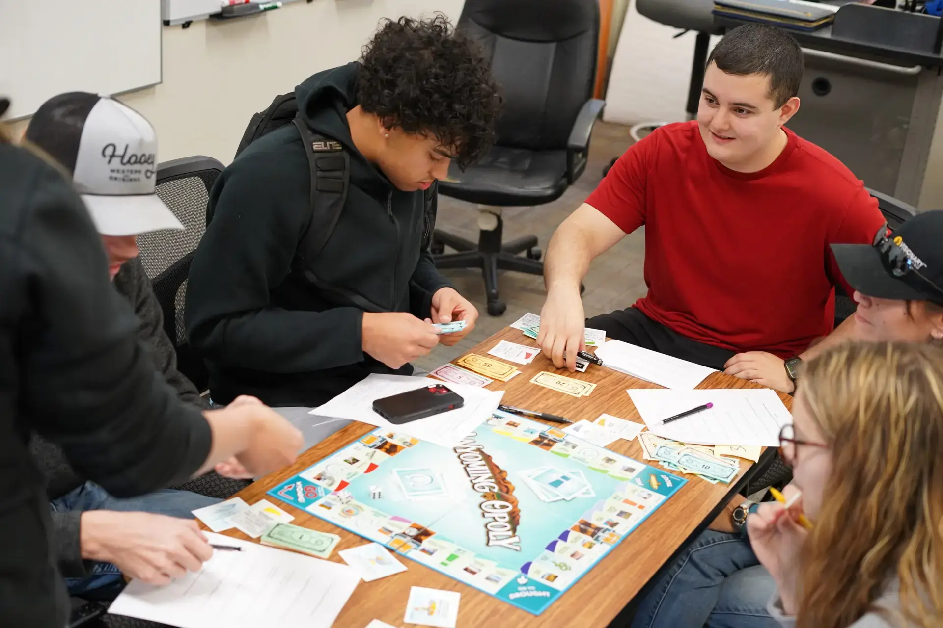 Students sitting around a table playing Monopoly counting fake money